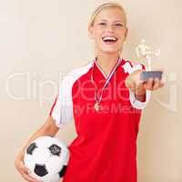 Winning comes easily to her. Portrait of a young woman dressed in a soccer uniform holding up a trophy and a soccer ball.