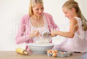 Mixing it all in with mum. A little girl sitting on a kitchen counter and helping her mother bake.