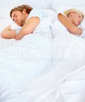 At odds with one another. A young couple sleeping back to back in bed.