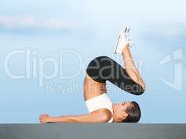 In complete control of her body. A young woman doing yoga outdoors against a blue sky.
