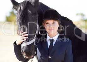 Horse and rider share a strong bond.... Portrait of a young female rider stroking her horses face and smiling proudly at the camera.