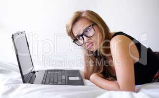 Technology frustrations. Shot of a beautiful young woman looking unsure while using a laptop on her bed.