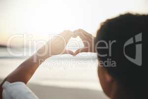 I love anything with a beautiful view. Rearview shot of a woman woman forming a heart against the horizon at the beach.