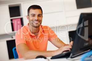 He enjoys his work. A smiling young entrepreneur working at his computer.