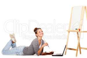 Im looking everywhere for inspiration. Shot of smiling young woman lying down by her laptop and a blank canvas on an easel.