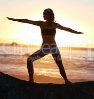 One last workout before sunset. Silhouette of a young woman doing a pilates pose at the beach.
