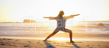 Tranquil and peaceful. Tranquil scene of a young woman doing a pilates pose on the beach at sunset.