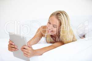 Browsing in comfort. A beautiful young blonde woman working on her digital touchpad while lying in bed.