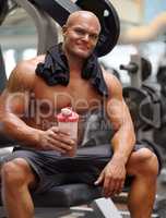Enjoying a protein shake after a workout. Portrait of a male bodybuilder holding a protein shake while sitting on a weight bench at the gym.
