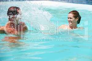 They have a playful relationship. Shot of a happy couple playfully splashing each other in a swimming pool.