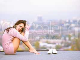 Playtime in the city. Young woman on a rooftop with her shoes off and the city in the background.