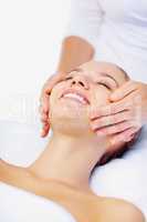 Happy female receiving a facial massage from a masseuse. Smiling young woman enjoying a massage while at a dayspa.