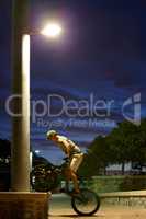 Never sleep - just ride. Shot of a man doing tricks on his bike at night under a street light.