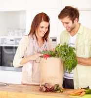 Lets pack these away. A happy couple in the kitchen with their newly-bought groceries.