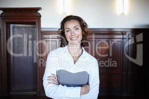 Ready for the judge. Attractive female legal person standing with her arms folded and smiling widely in the courtroom.