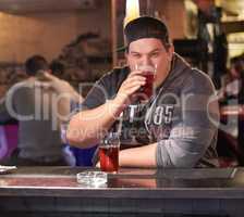 He enjoys a cold beer every Friday after work. Portrait of a young man drinking at the local bar.