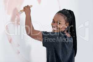 Nothing gives your house personality like a colourful paint job. Shot of a young woman painting a wall pink.