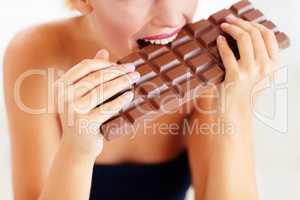 Nothing but sinful indulgence. Cropped view of a young woman biting into a big slab of chocolate.