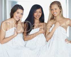 Hiding behind the sheets. Three attractive young females holding a bed sheet over their naked bodies.