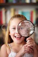 Magnify it. A little blonde girl looking through a magnifying glass.