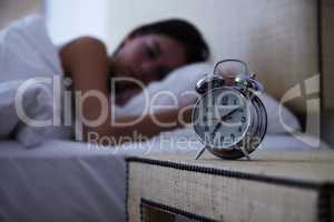 Sleeping the day away. A young woman sleeping with her alarm clock next to her bed.