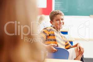 Get the attention of the cool kid in class. Smiling young boy turning round in class to look at a classmate - copyspace.