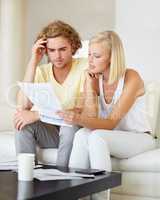 Where are all these bills coming from. A young couple reading a financial statement together in their lounge.