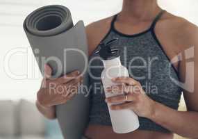 Replace sweat with water. Cropped shot of an unrecognizable woman standing alone at home and holding a yoga mat and a bottle of water.