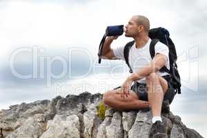 Taking the road less travelled. A young man taking a break from hiking while sitting on a rock and drinking some water.