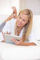 Going online in comfort. A beautiful young blonde woman working on her digital touchpad.