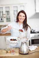 Fruit Scoop. An attractive woman adding fruit to a blender while standing at a kitchen counter.