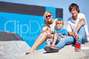 Teaching him to be styling. Portrait of a two young teens and a little boy sitting outside at a skate park.