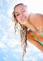 Lovely young female in bikini against the cloudy sky. Upward view of a cute female in bikini smiling at you against the cloudy sky.