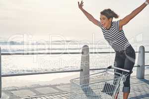 Im just out here living my best life. Shot of a young woman riding a shopping cart on the promenade.