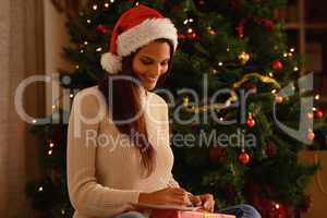 Thinking about all the presents. A young woman writing in a christmas card in front of a christmas tree.