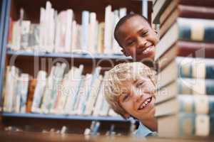Hello. Two school friends peering around a stack of books in the library.