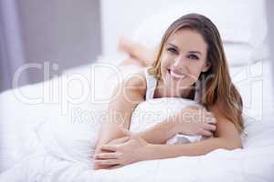 Comfortable in bed. A gorgeous brunette woman smiling comfortably in bed at home.