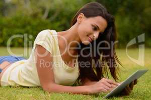 Connection in comfort. A young woman working on a touchpad while lying on the grass.