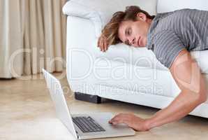 High-speed connection for couch potatoes. A young man lying on his couch with his hand resting on his laptops keyboard.