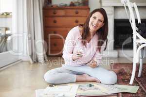 Shes enjoying her new hobby. A smiling woman working on a scrapbook while sitting on the floor in a home interior.