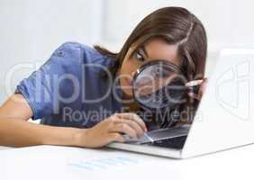 Not missing a speck of dirt.... Young woman using a magnifying glass while cleaning her laptop keyboard.