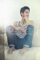 Moments to reflect. A young attractive male sitting casually with his feet up on a sofa contemplating - Copyspace.