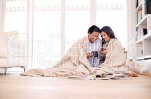 Making the most of their time together. Shot of a young couple sitting on the floor wrapped in a blanket looking at photo albums.