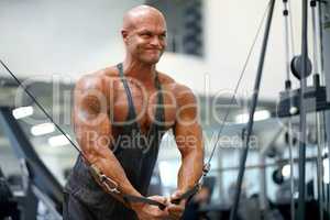 Working hard to reach his goals. A male bodybuilder using exercise equipment to train at the gym.