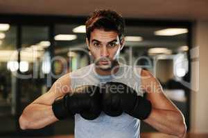 Fiercely focused competitor. Portrait of a focused man wearing boxing gloves and sport clothing posing ready to fight at the gym.