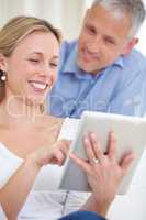 Check out these features. An attractive young woman using her digital tablet with her husband standing behind her.