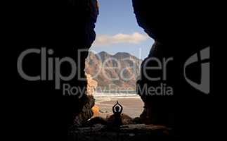Yoga opens the mind to beautiful things. Shot of a woman practising yoga while sitting in a cave overlooking the sea.
