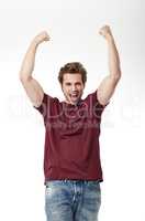 Awesomeness personified. Studio shot of a young man in jeans and t-shirt with his arms raised in victory.