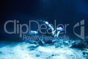 Braving the depths of the dark ocean. Male scuba diver floating just off the ocean bottom - Deep ocean diving.