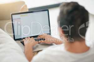 Connect and catch up with the world. Rearview shot of a relaxed young man using a laptop on the sofa at home.